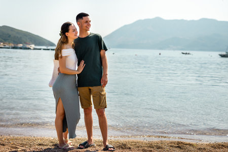 Young couple stands on the beach gazing into the distance, with the girlfriend resting her head gently on her boyfriend's chest.の写真素材