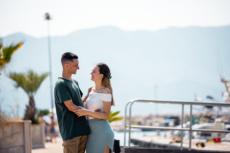 A young couple on summer vacation stands by the marina deck, holding each other closely and gazing into each otherâs eyes.の写真素材