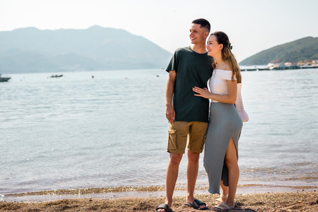 Young couple stands on the beach gazing into the distance, with the girlfriend resting her head gently on her boyfriend's chest.の写真素材