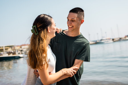 Young couple stands on the beach, embracing and smiling joyfully as they enjoy the beauty of the sea.の写真素材