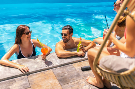 A group of young people hang out by the pool, some with legs in the water, enjoying colorful...