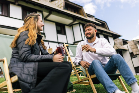 A young man and woman relax on lounge chairs during a weekend getaway at a mountain resort. Surrounded by nature and fresh air, they savor hot coffee and refreshing juice.の写真素材