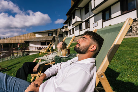 A young man and woman relax on lounge chairs at a mountain resort during a sunny weekend escape.