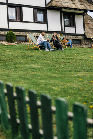 A young man and woman relax on lounge chairs during a weekend getaway at a mountain resort. Surrounded by nature and fresh air, they savor hot coffee and refreshing juice.の写真素材