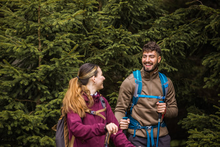 A young man and woman equipped with backpacks, hiking poles, and hiking clothes carefully navigate a...
