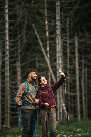 A young man and woman, fully equipped with backpacks, hiking poles, and hiking clothes, pause on a...