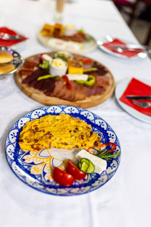ull Serbian breakfast table with assorted meza, scrambled eggs with bacon, fried egg with sausages,...
