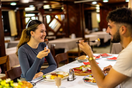 A couple eating breakfast at a resort restaurant table, featuring eggs, ham, fresh vegetables, and traditional morning dishes in a relaxed vacation setting.の写真素材