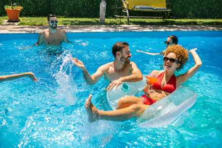 Young couple enjoying colorful cocktails in the pool on a sunny day; the afro-haired girl is on a...