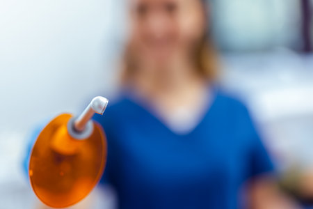 Female dentist in blue coat holding curing light for dental treatment. Close-up in modern dental clinic. Concept of care, precision, and dental procedure.の写真素材