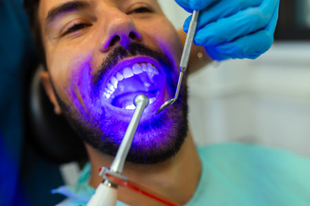 Female dentist treating male patientâ€™s teeth using curing light in modern dental clinic.