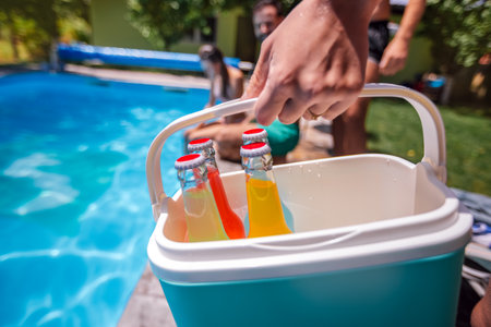 Close-up of a hand holding a small cooler with colorful cocktails, bringing drinks to a group of...