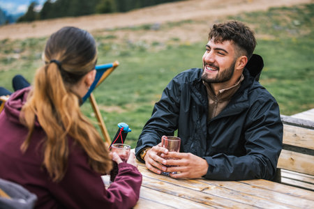 Two hikers relax in a mountaintop restaurant after a hike, enjoying a stunning panoramic view of...