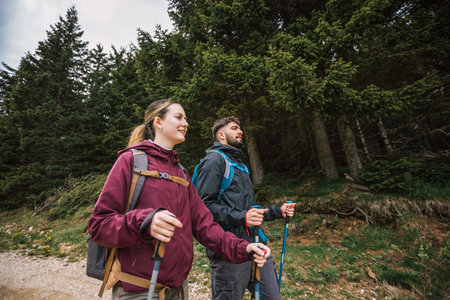 Male and female hikers with full gear trek through stunning mountains, wearing boots, backpacks, and jackets, surrounded by breathtaking nature.の写真素材