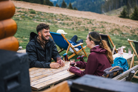 Two hikers relax in a mountaintop setting after a hike, drinking and enjoying a stunning panoramic view of nature.の写真素材