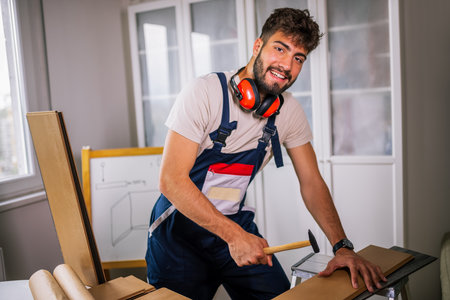 Repairman with full equipment hammers laminate flooring in an apartment, ensuring precise installation and high-quality craftsmanship.の写真素材