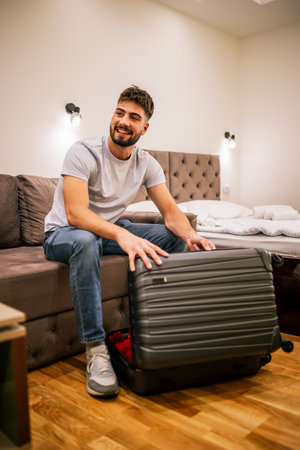 Man on a trip, in his hotel room, unpacking clothes from his suitcase and organizing his belongings indoors.の写真素材