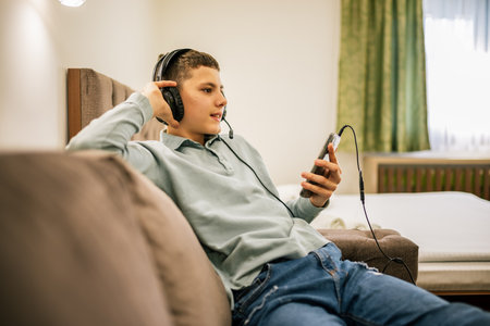 Young boy wearing headphones and enjoying music on his smartphone, relaxing indoors.