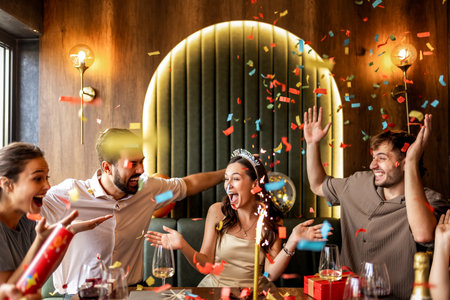 Group of friends celebrate a birthday in a restaurant, dancing and throwing confetti, enjoying fun, laughter, and festive moments together.の写真素材