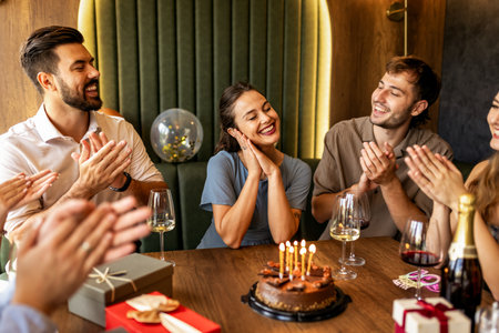 Happy friends sing the birthday song in a restaurant with cake, presents, wine, and laughter,...