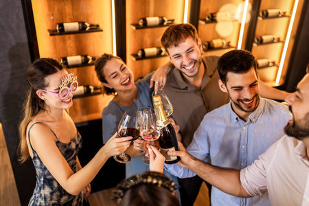 Friends celebrate a birthday in a restaurant, standing and dancing with wine glasses and balloons, cheering together and sharing joyful moments.の写真素材
