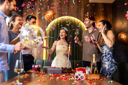 Group of friends celebrate a birthday in a restaurant, dancing and throwing confetti, enjoying fun, laughter, and festive moments together.の写真素材