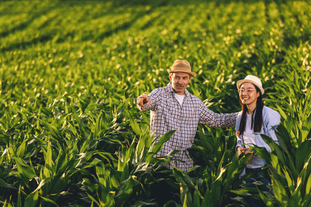 Two farmers stand in a spacious corn field, looking into the distance. The scene reflects...