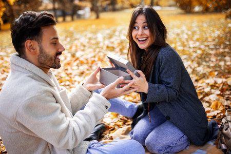 Romantic young couple giving presents to each other in colorful autumn park, joyful and loving fall...