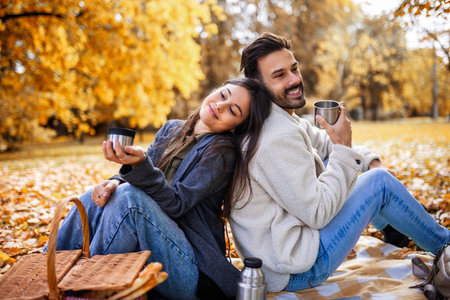 Relaxed young couple enjoying coffee together in colorful autumn park, romantic and cozy fall...