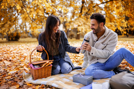 Relaxed young couple enjoying coffee together in colorful autumn park, romantic and cozy fall...