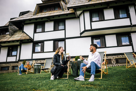 Happy young couple enjoying coffee and juice on loungers in front of hotel during autumn, peaceful and romantic fall getaway.の写真素材
