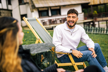Happy young couple enjoying coffee and juice on loungers in front of hotel during autumn, peaceful...