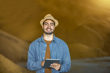 Young man stands in warehouse in front of large soybean pile holding tablet, concept of modern agricultureの写真素材