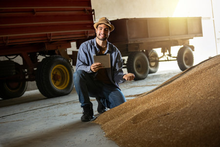 Young man holds soybeans in one hand and tablet in the other in warehouse, concept of modern agriculture, crop management, farming, logistics, food industry.の写真素材