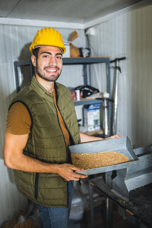 Young agricultural worker inspecting and collecting wheat samples before storage at grain facility, ensuring quality and proper handling.の写真素材