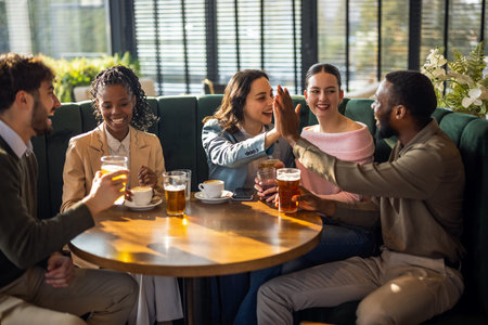 Smiling friends clapping hands while having beer at bar counter in pubの写真素材