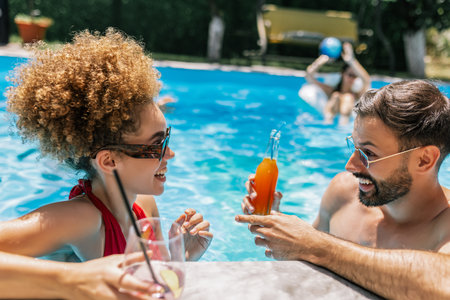 cheerful multiethnic friends drinking cocktails in swimming pool at summer