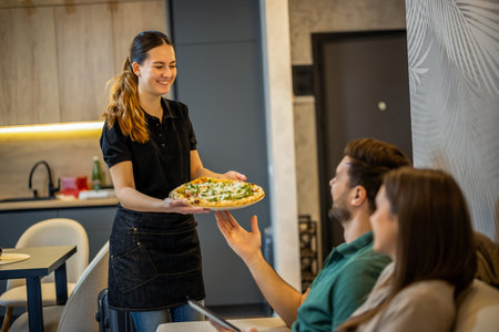 Smiling waitress serving pizza to couple in cafe. Food delivery conceptの写真素材