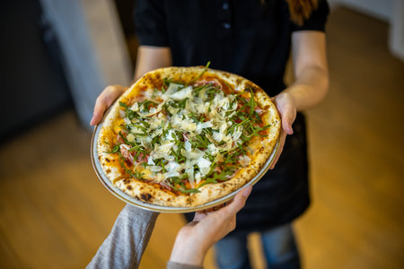 Female hands holding a pizza with ham, onion, cheese and herbsの写真素材
