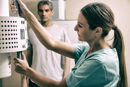 Young female doctor checking x-ray machine before a male patient scan.の写真素材