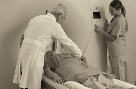 Senior male doctor and female assistant examining woman in 70s with CT scanner.