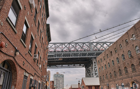 Metallic structure of Manhattan Bridge among classic Brooklyn buildings, New York City.のeditorial素材