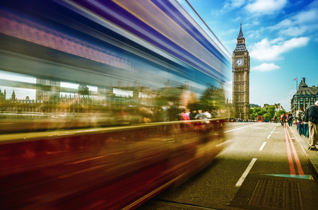 Red Double Decker bus moving on Westminster Bridge with Big Ben on background - London.