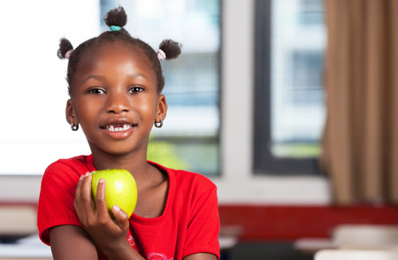 African girl at school desk ready to eat her apple.の写真素材