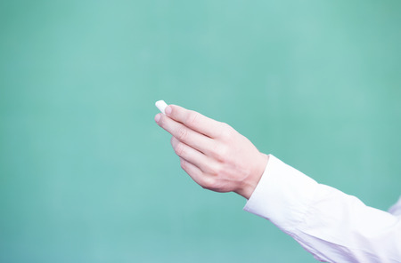 Female teacher hand holding chalk in front of empty blackboard.
