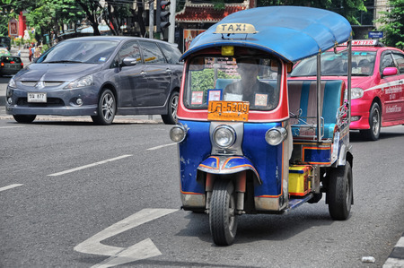 BANGKOK - AUG 23: A three wheeled tuk tuk taxi transports passengers along road, August 23, 2012 in...
