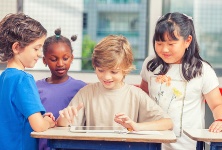 Multicultural classroom playing with tablet at school. Happiness and togetherness concept.の写真素材