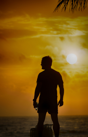 Silhouette of man standing on the beach with water bottle.の写真素材