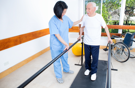 Elder retired man assisted by nurse in rehab clinic.の写真素材