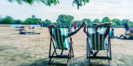 Couple laying on beach chairs in a city park, back view.の写真素材